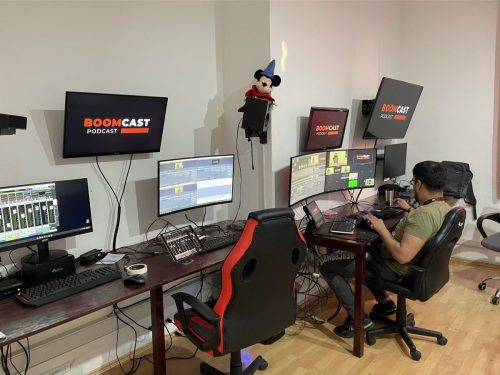 Estación de control de producción audiovisual con múltiples monitores, consolas de audio y video, y operador monitoreando la postproducción de un podcast en estudio.