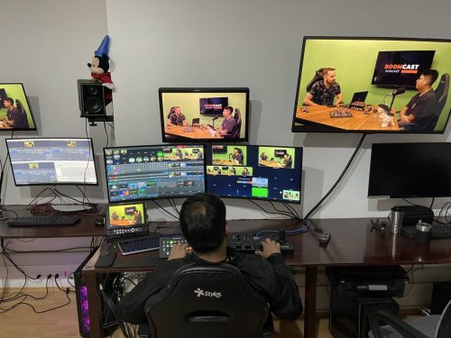 Mesa de control de producción en vivo con múltiples monitores multi-view y operador técnico gestionando la transmisión de un podcast o evento híbrido.