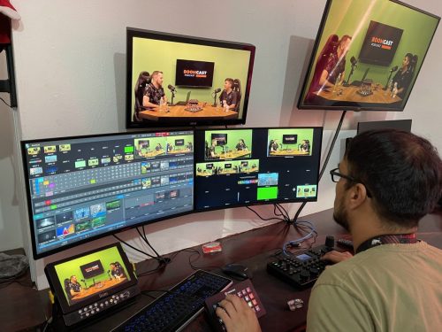 Mesa de control de producción en vivo con operador manejando switcher de video y múltiples monitores para la transmisión de un podcast o evento híbrido.