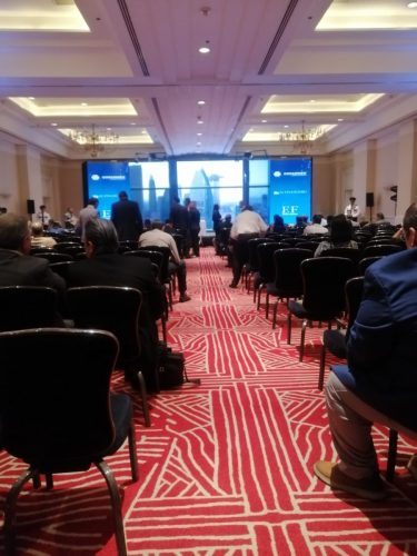 Salón de conferencias con montaje tipo auditorio lleno de asistentes durante un evento corporativo con pantallas al fondo.