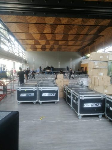 Montaje de evento audiovisual en salón amplio con cajas de transporte profesional (flight cases) y personal instalando el escenario al fondo.